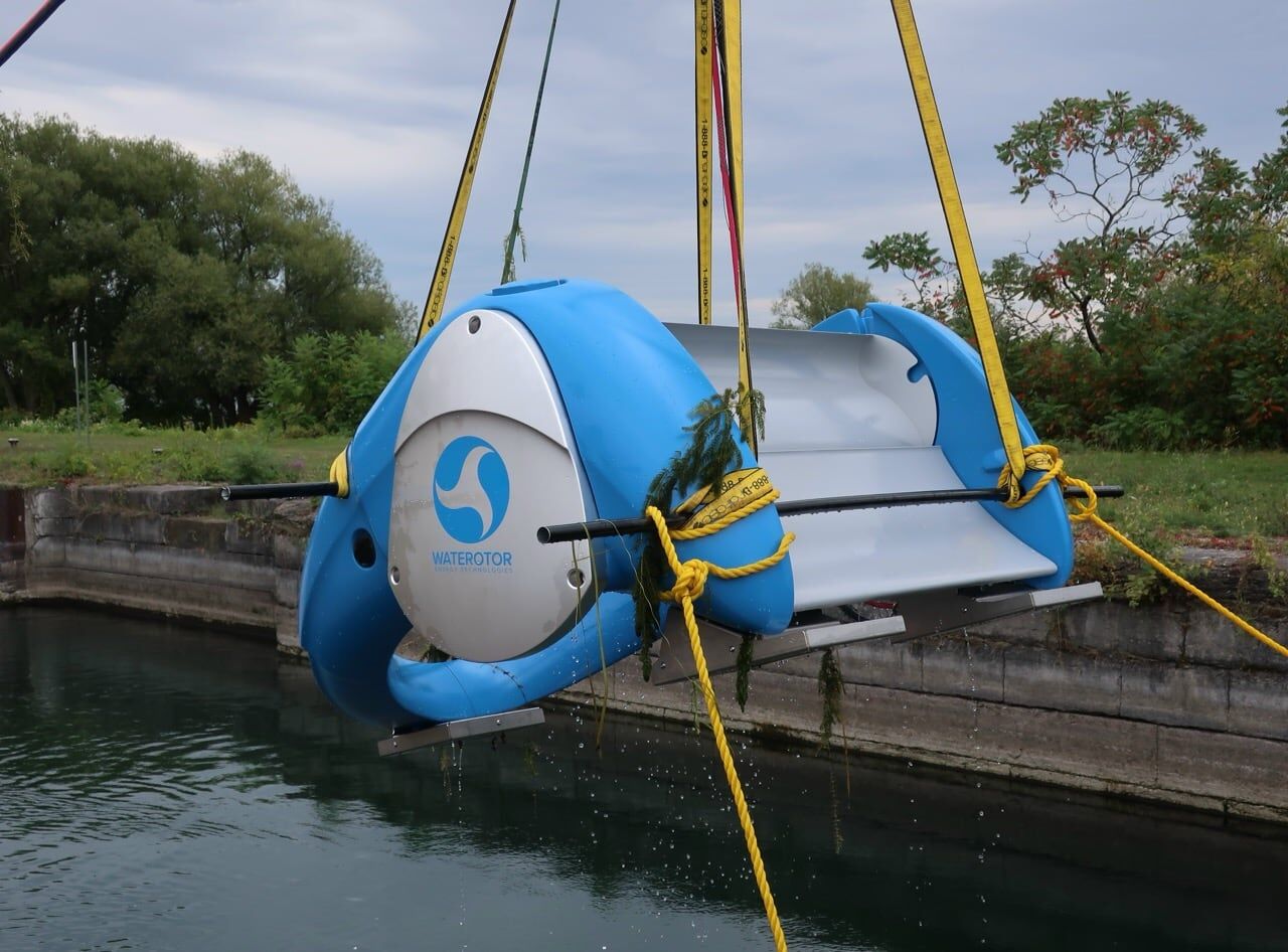 A blue Waterotor unit lifted by straps into a concrete-walled canal
