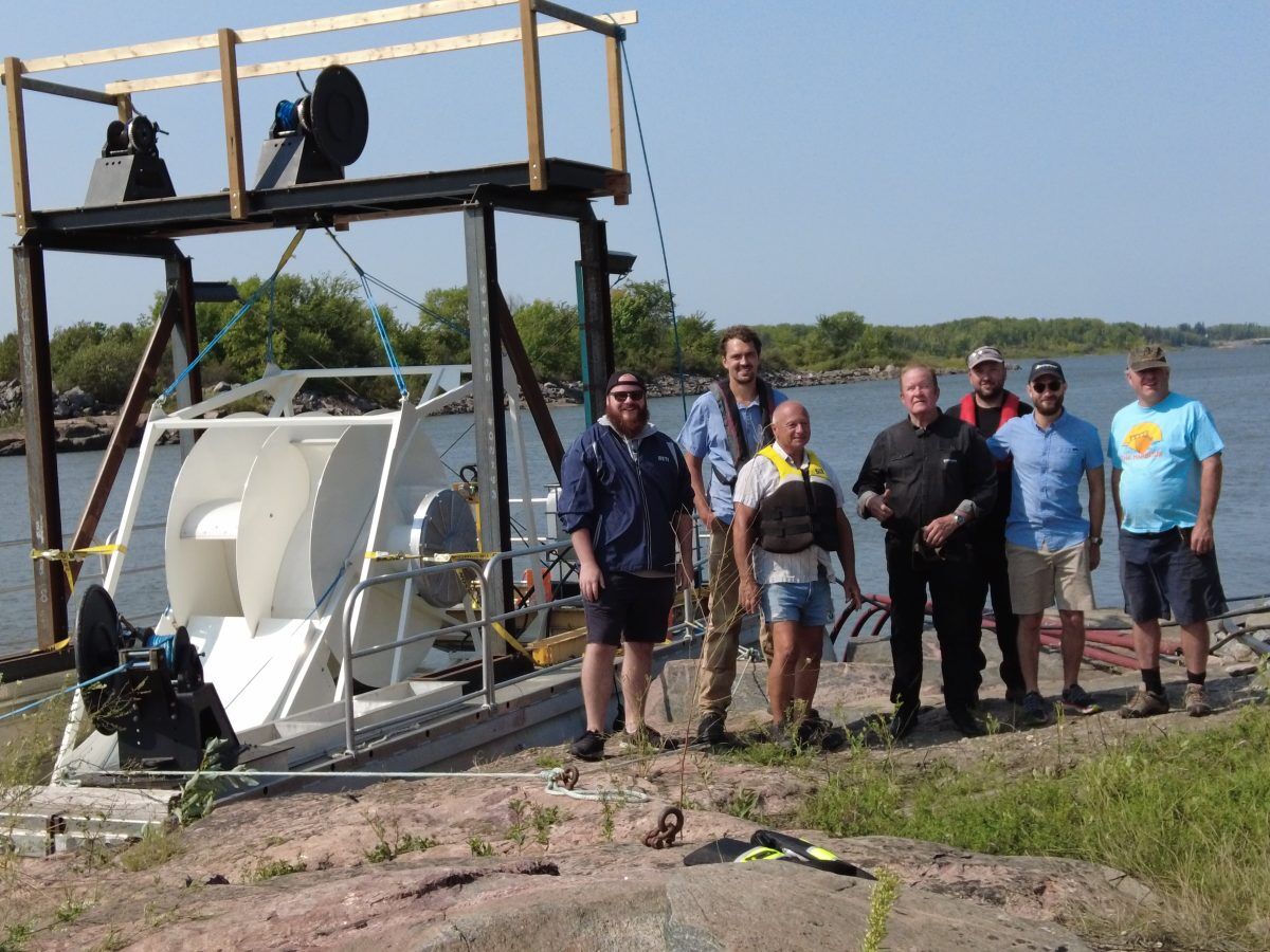 The Waterotor crew standing on a riverbank next to the test barge
