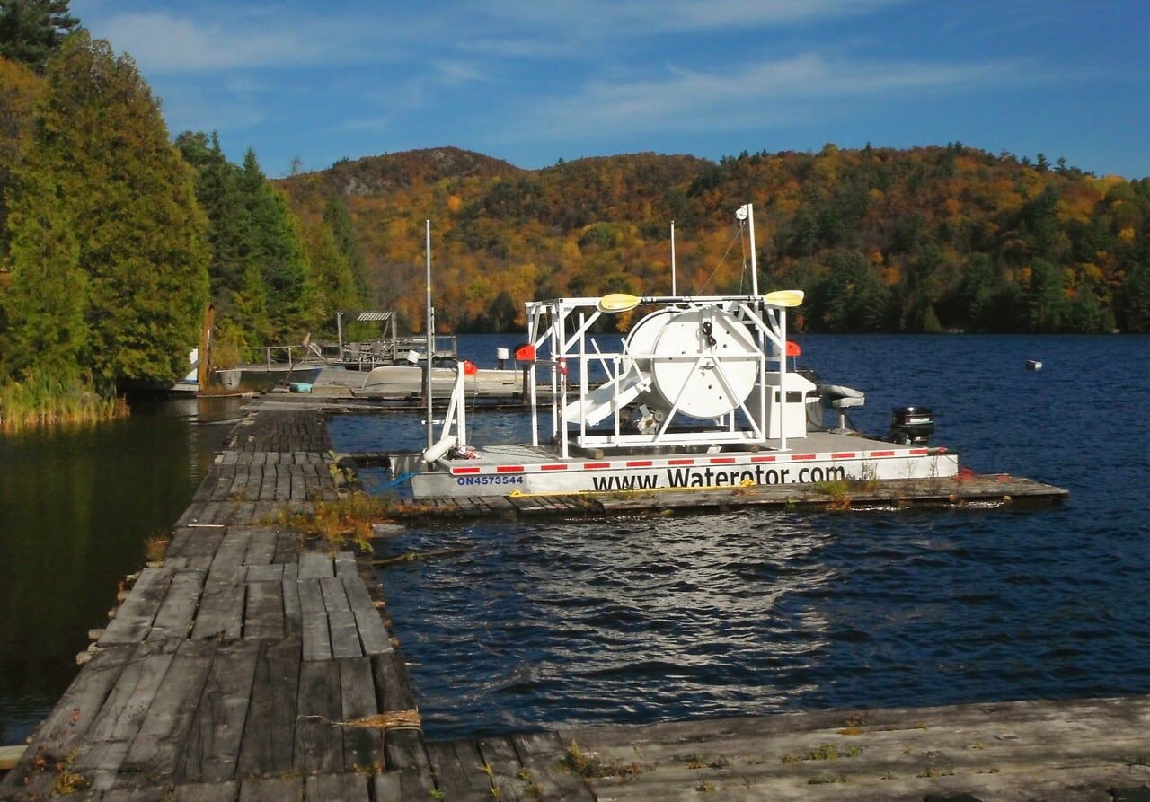 Waterotor test platform moored at a wooden dock on a river lined with autumn forest