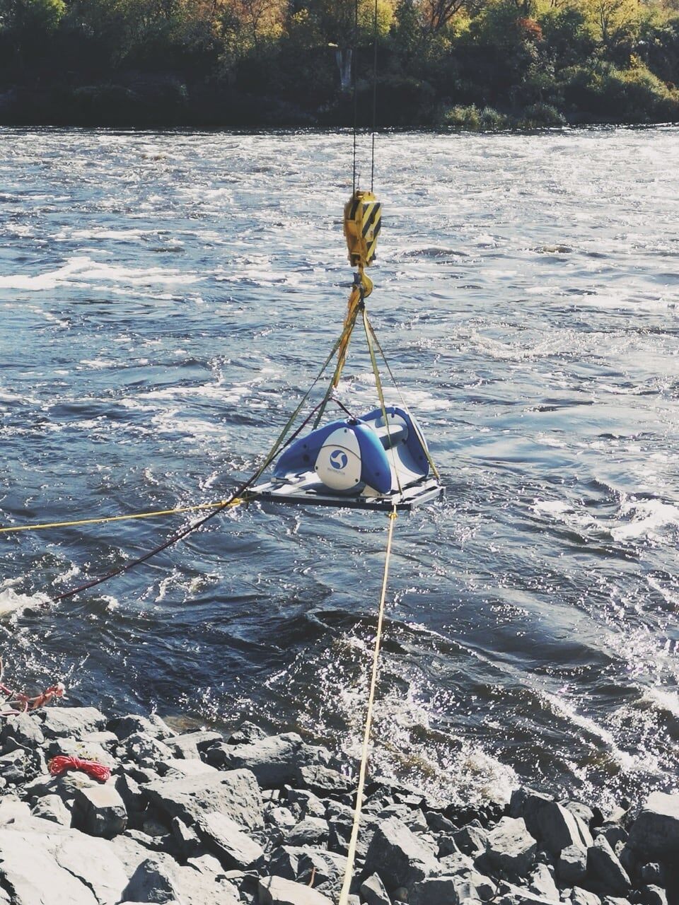 Drone view of a Waterotor being lowered by cable into fast river water