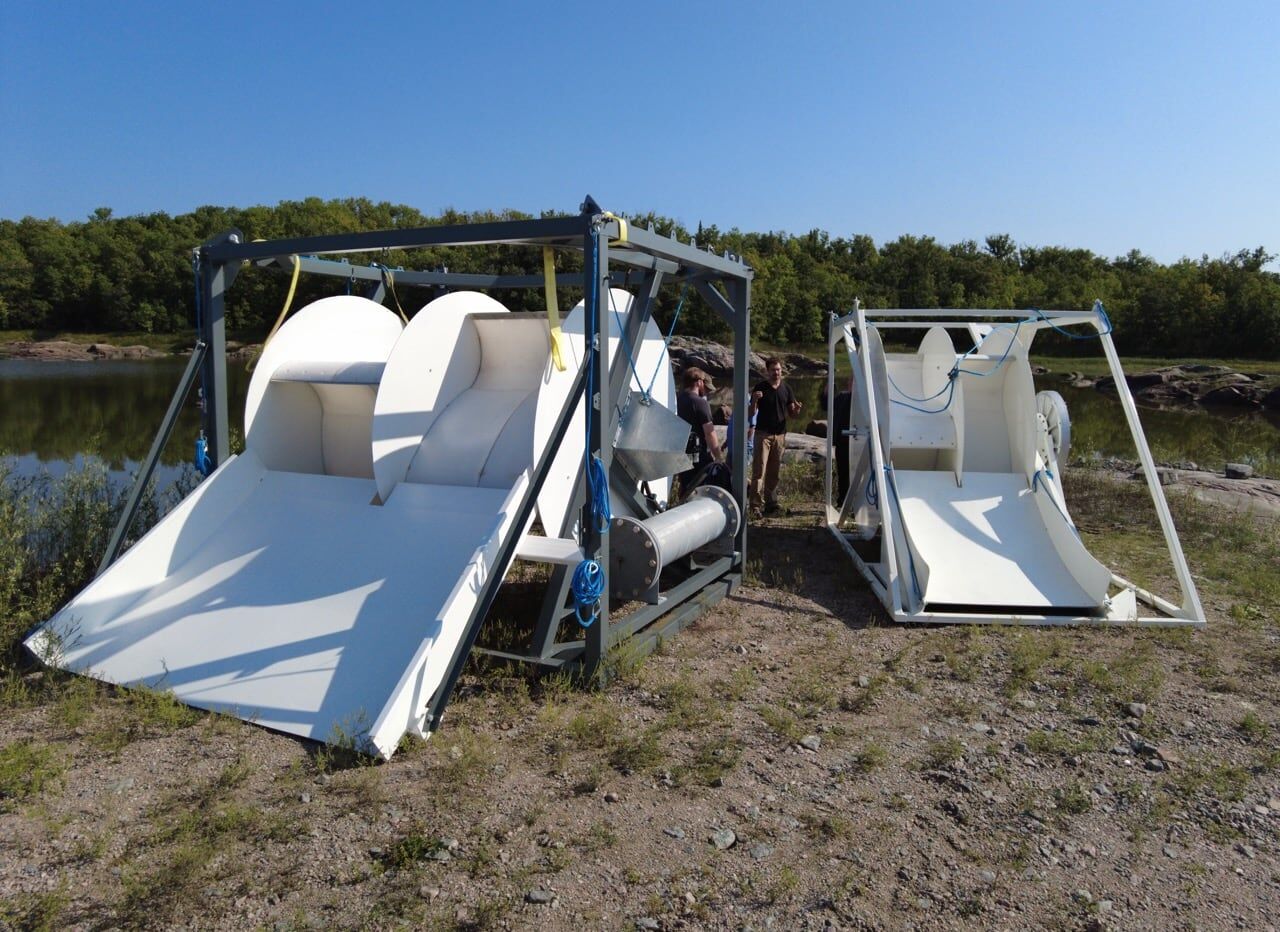 Two white Waterotor rotors on the grassy shore of a river